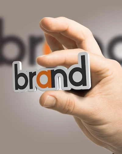 Top Brand Name Suggestion Agency in Gandhipuram, Coimbatore A hand holding a 'brand' word which is in black & orange colour,'a' letter alone coloured in orange